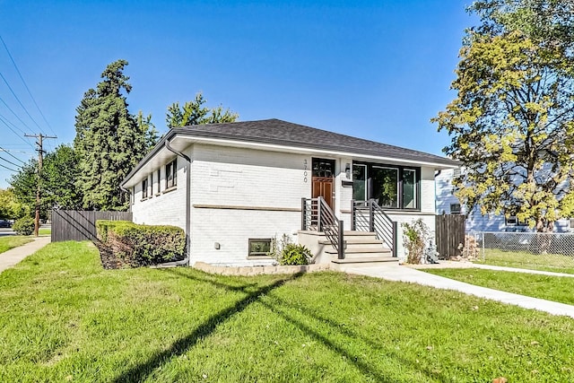 view of front of property featuring brick siding, fence, a front lawn, and roof with shingles