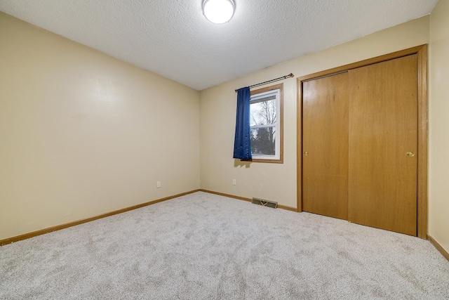 unfurnished bedroom featuring a closet, visible vents, carpet flooring, a textured ceiling, and baseboards