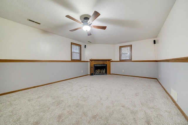 unfurnished living room with carpet flooring, a fireplace with flush hearth, visible vents, and baseboards