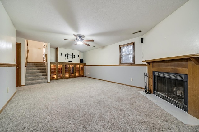 unfurnished living room with visible vents, a fireplace with flush hearth, carpet flooring, a textured ceiling, and stairs