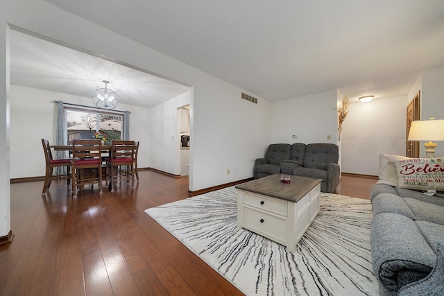 living room featuring visible vents, dark wood finished floors, a notable chandelier, and baseboards