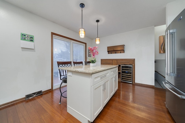 kitchen with a breakfast bar area, wood-type flooring, visible vents, white cabinets, and high quality fridge