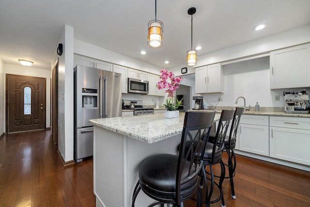 kitchen with a kitchen island, light stone counters, appliances with stainless steel finishes, a breakfast bar, and dark wood-type flooring