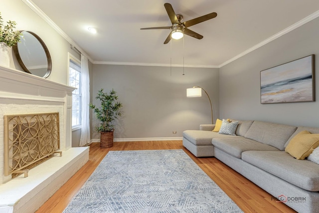 living room with baseboards, ornamental molding, a ceiling fan, a fireplace with raised hearth, and wood finished floors