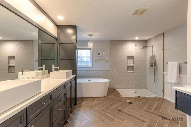 bathroom with double vanity, walk in shower, visible vents, a freestanding bath, and a sink
