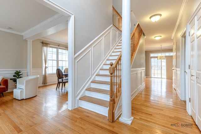 stairway with a decorative wall, wood finished floors, ornamental molding, and decorative columns
