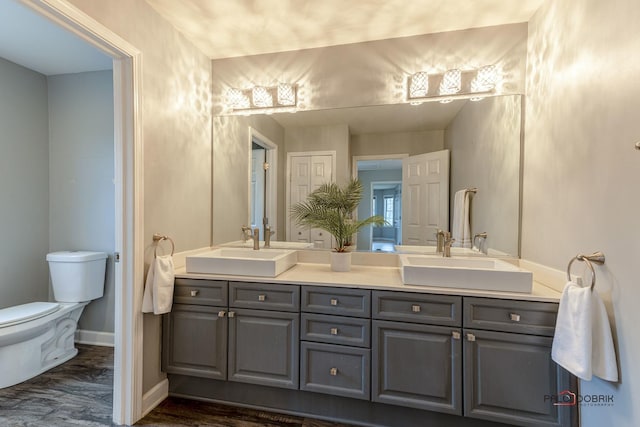 full bath featuring a sink, toilet, double vanity, and baseboards