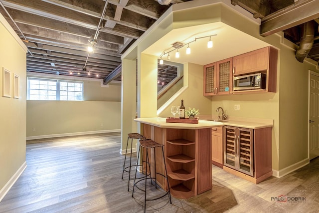 bar featuring a sink, wet bar, stainless steel microwave, light wood finished floors, and beverage cooler