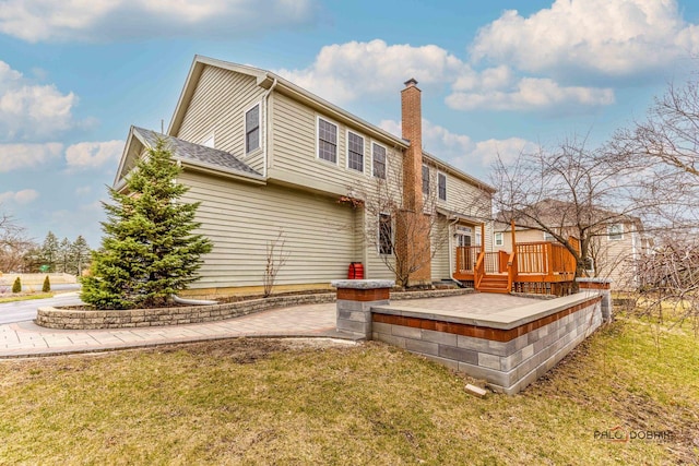 rear view of property featuring a chimney, a deck, and a lawn