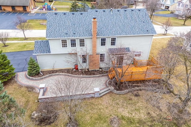 back of house with a deck, a chimney, a shingled roof, and a playground