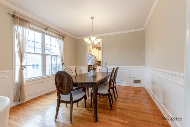 dining space featuring light wood-type flooring, a chandelier, crown molding, visible vents, and a decorative wall