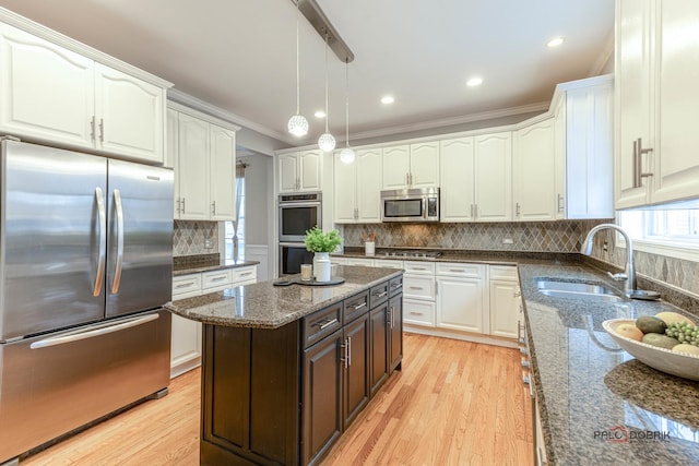 kitchen featuring white cabinets, appliances with stainless steel finishes, a sink, decorative light fixtures, and light wood finished floors