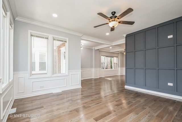 empty room featuring a ceiling fan, crown molding, a decorative wall, and wood finished floors