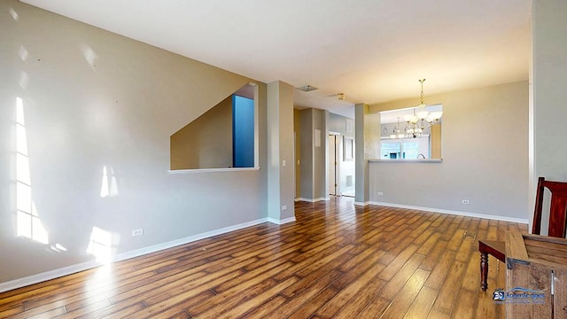 unfurnished living room featuring a notable chandelier, baseboards, and hardwood / wood-style flooring