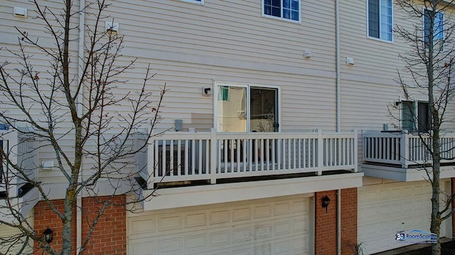 rear view of property featuring brick siding, a balcony, and an attached garage