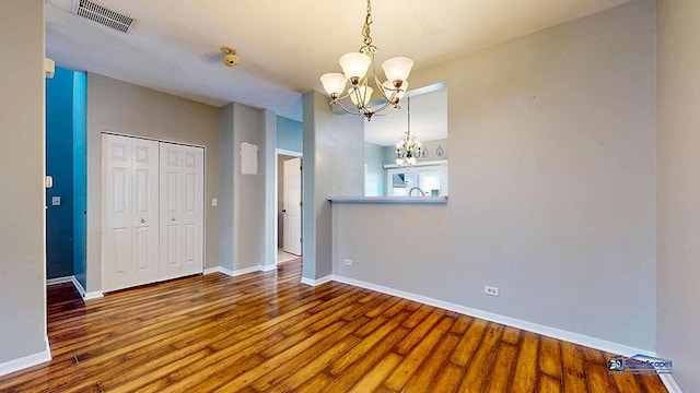 unfurnished room with a notable chandelier, wood finished floors, visible vents, and baseboards