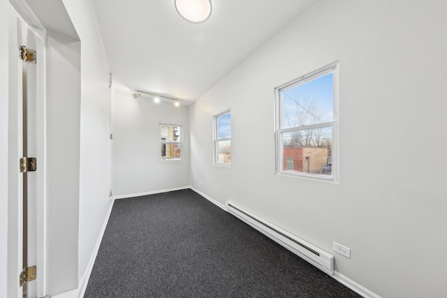 spare room with a baseboard heating unit, dark colored carpet, track lighting, and baseboards