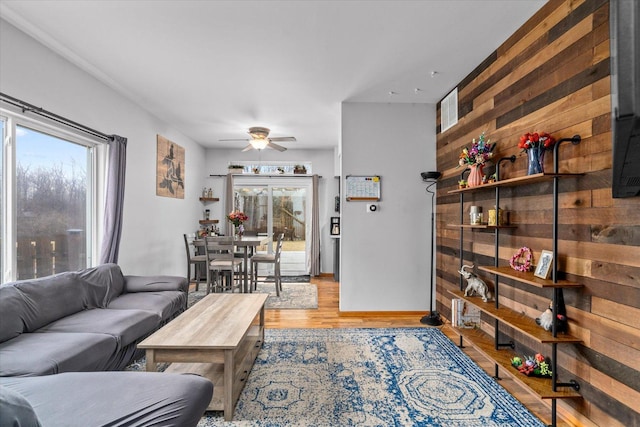 living area with wood walls, plenty of natural light, a ceiling fan, and wood finished floors