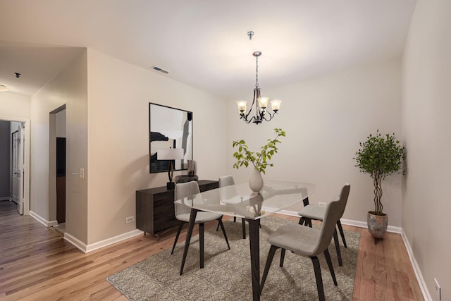 dining area with baseboards, light wood-type flooring, visible vents, and a notable chandelier