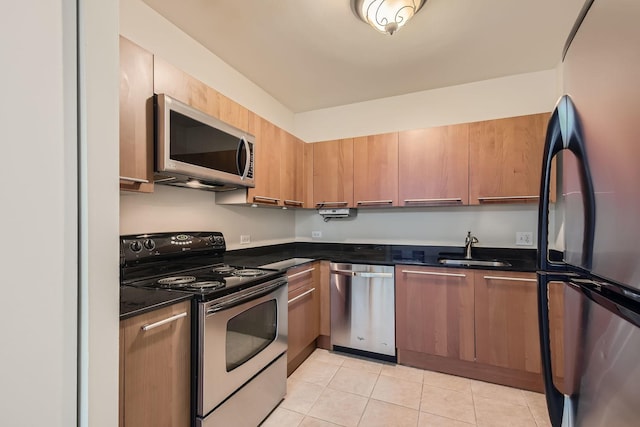 kitchen with dark countertops, light tile patterned floors, appliances with stainless steel finishes, and a sink