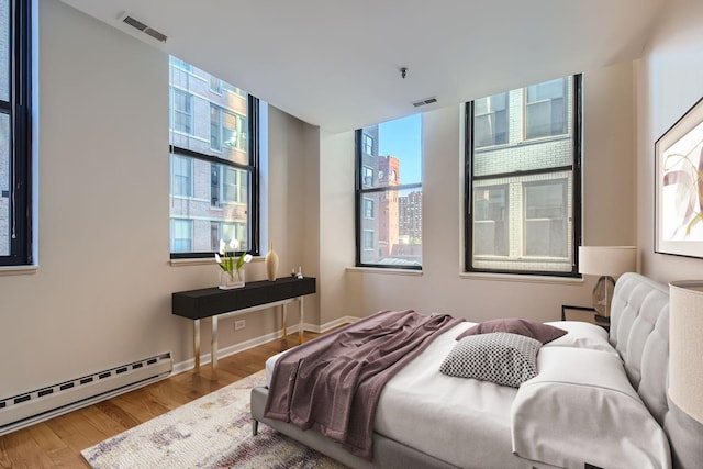 bedroom with baseboards, visible vents, baseboard heating, and wood finished floors