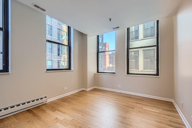 spare room with light wood-style floors, visible vents, a baseboard heating unit, and baseboards