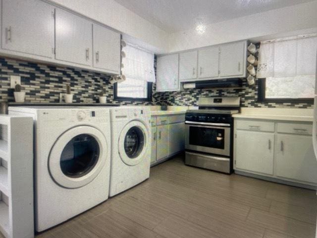 kitchen with wood finished floors, independent washer and dryer, under cabinet range hood, stainless steel range with electric stovetop, and backsplash