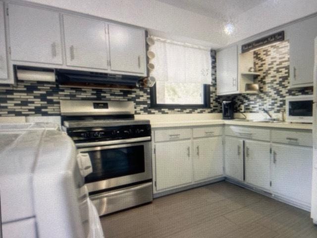 kitchen with tasteful backsplash, stainless steel range, light countertops, and ventilation hood