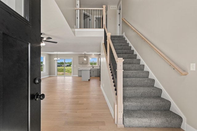 foyer featuring visible vents, light wood finished floors, baseboards, stairs, and ceiling fan with notable chandelier