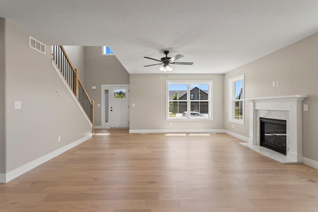 unfurnished living room featuring visible vents, light wood-style floors, a fireplace, and stairway