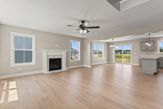 unfurnished living room with light wood-type flooring, baseboards, a high end fireplace, and ceiling fan with notable chandelier