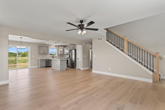 unfurnished living room featuring light wood-type flooring, baseboards, stairs, and ceiling fan with notable chandelier