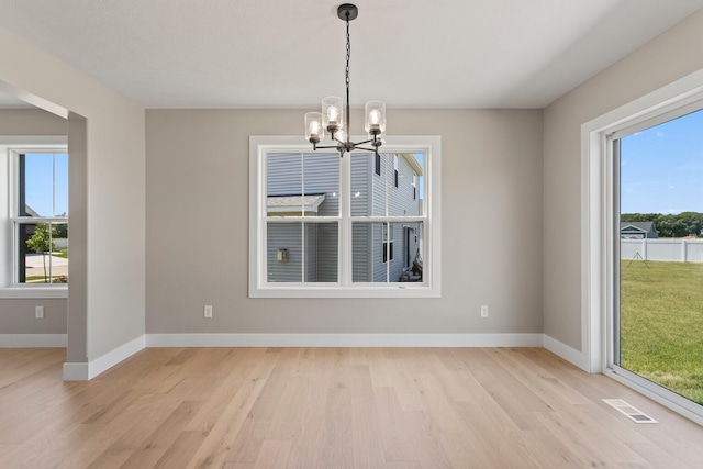 unfurnished dining area with a chandelier, visible vents, light wood-style floors, and baseboards