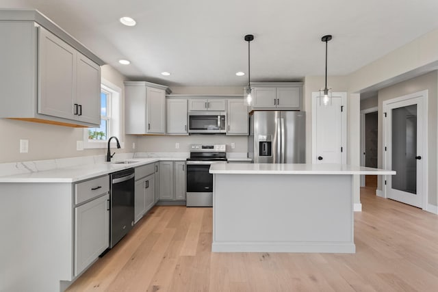 kitchen with light wood-style flooring, gray cabinets, a sink, a kitchen island, and stainless steel appliances