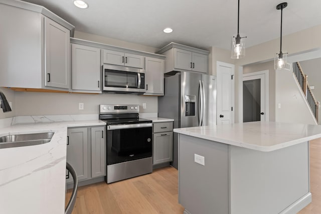 kitchen with a sink, light wood finished floors, appliances with stainless steel finishes, and gray cabinetry