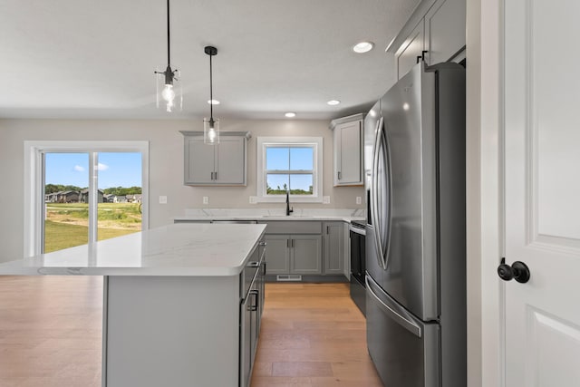 kitchen with a kitchen island, gray cabinets, freestanding refrigerator, a sink, and light wood-type flooring