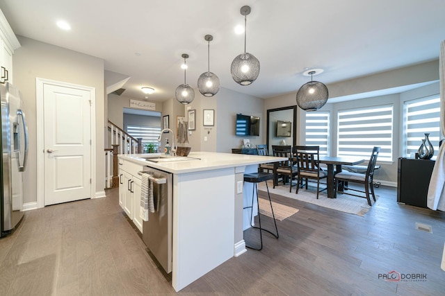 kitchen with wood finished floors, a center island with sink, a sink, appliances with stainless steel finishes, and white cabinetry