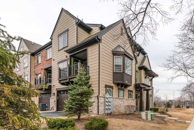 view of property exterior featuring aphalt driveway, stone siding, a garage, and central AC