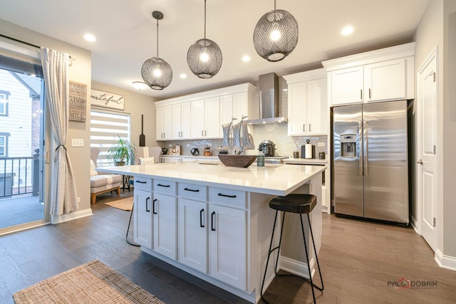 kitchen with a kitchen island, stainless steel fridge, wall chimney exhaust hood, white cabinets, and light countertops