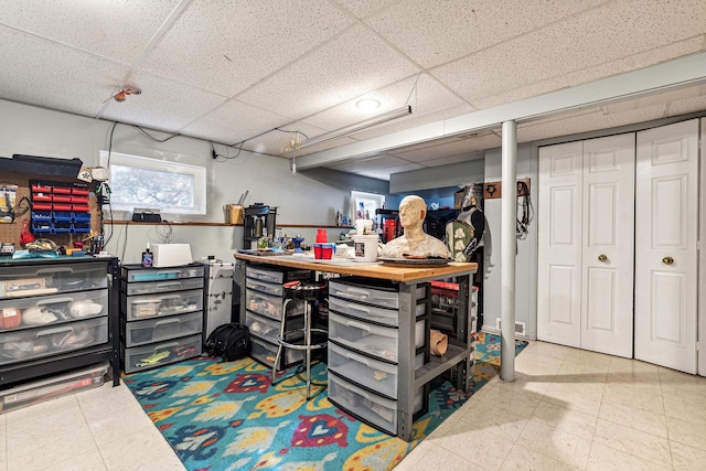 below grade area with a paneled ceiling, tile patterned floors, and a workshop area