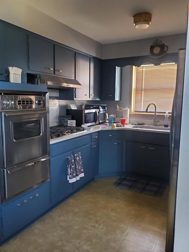 kitchen featuring appliances with stainless steel finishes, light countertops, under cabinet range hood, a sink, and a warming drawer