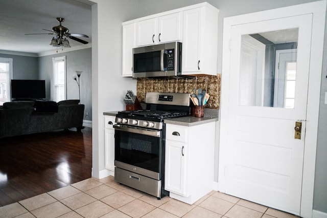 kitchen featuring stainless steel appliances, decorative backsplash, ornamental molding, white cabinets, and light tile patterned flooring