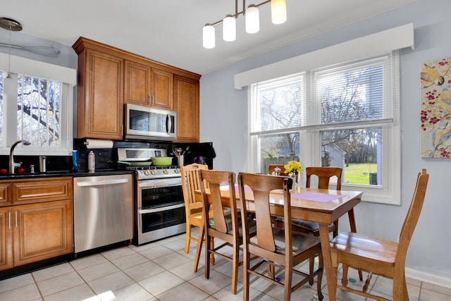 kitchen with brown cabinets, stainless steel appliances, dark countertops, light tile patterned flooring, and a sink