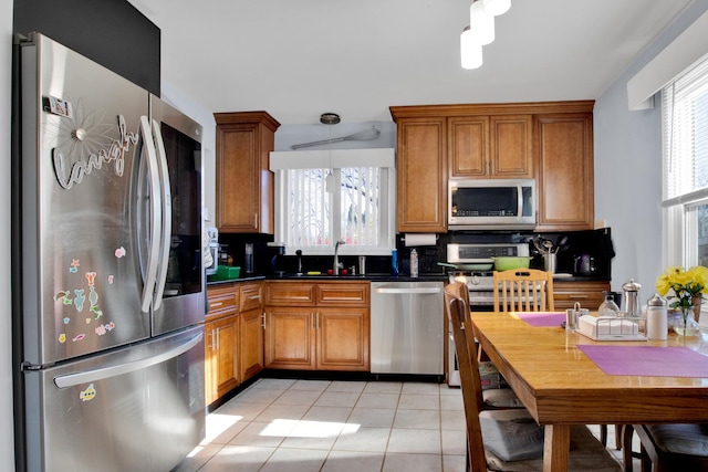 kitchen featuring brown cabinetry, dark countertops, stainless steel appliances, a sink, and light tile patterned flooring
