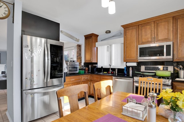 kitchen with light tile patterned floors, brown cabinetry, dark countertops, appliances with stainless steel finishes, and a sink