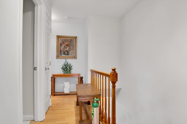hall with light wood-style flooring and an upstairs landing