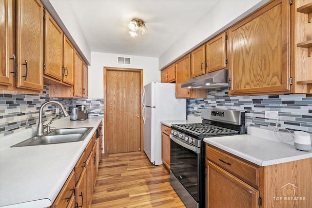 kitchen featuring a sink, under cabinet range hood, stainless steel range with gas stovetop, light countertops, and open shelves