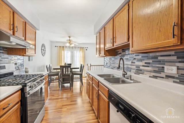 kitchen with light countertops, under cabinet range hood, light wood finished floors, dishwashing machine, and stainless steel gas range