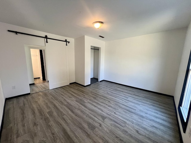 unfurnished bedroom featuring wood finished floors, baseboards, a closet, and a barn door
