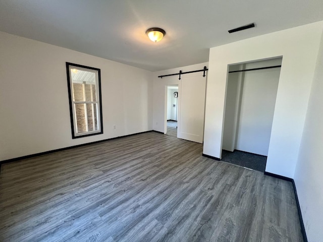 unfurnished bedroom with a closet, visible vents, a barn door, baseboards, and dark wood-style floors